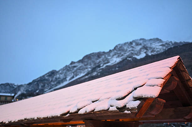 Cosy and romantic wooden cabin on a snowy mountain with a clear blue sky.