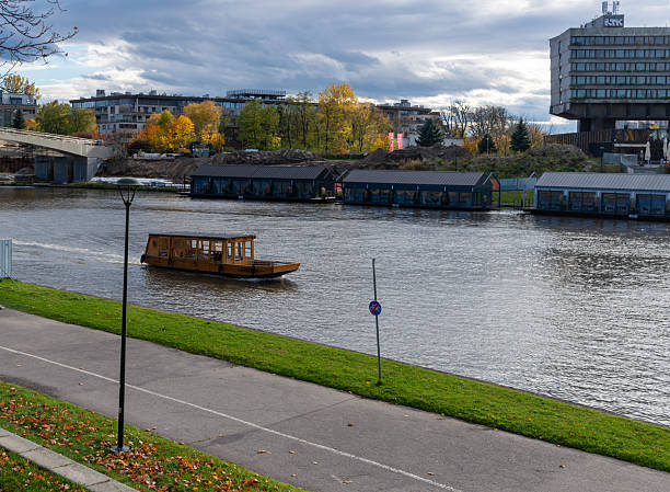 Krakow, Poland – October 25, 2025: A small wooden passenger boat moves slowly along the Vistula River, passing riverside paths and floating buildings during a quiet autumn afternoon in the city.