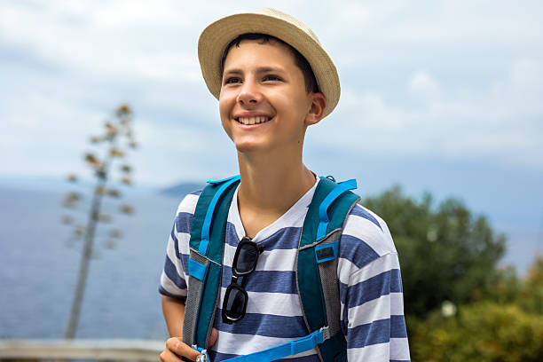 Teenage boy hiking along a coastal trail with sea view and a flowering agave tree in the background. Summer adventure, outdoor exploration, and scenic travel lifestyle.