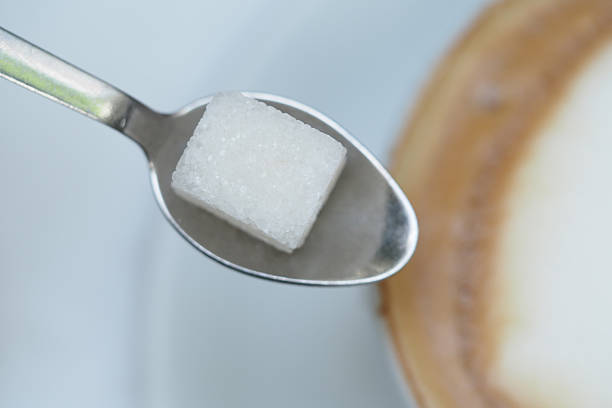 A sugar cube sits on a spoon near a cup of coffee, ready to sweeten.