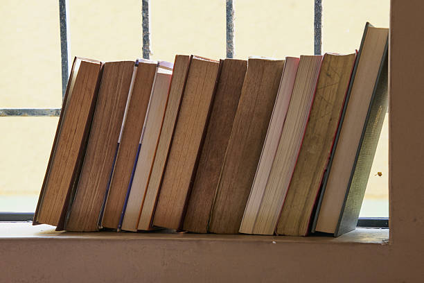 A group of books leaning against a wall at the foot of a window