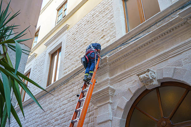 Man on Ladder Protecting Wooden House Exterior  Applying Paint with Paintbrush