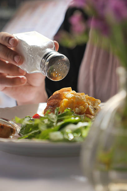 Adding seasoning to a fresh salad on a dining table