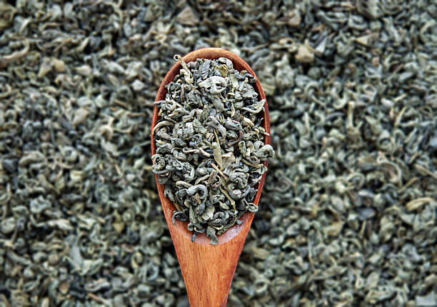 Macro view of dried rolled green tea leaves on a wooden spoon with bokeh background, showing texture for wellness, tea culture, and herbal concepts.