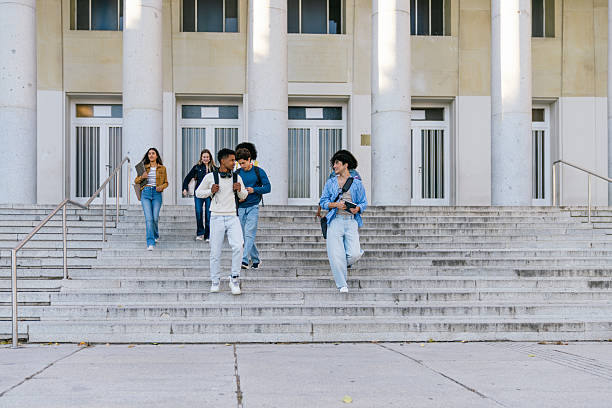 Students walking on campus stairs holding books. Represents youth, friendship, and university life in an urban setting.