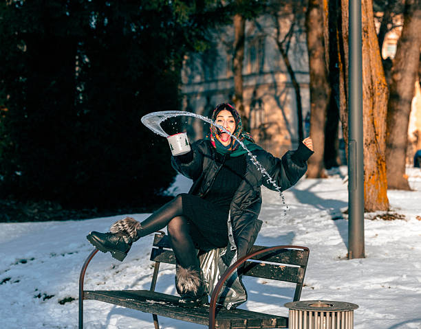 Female enjoying winter activities, sitting on a bench in a snowy park, playfully interacting with snow, creating a lively and cheerful atmosphere
