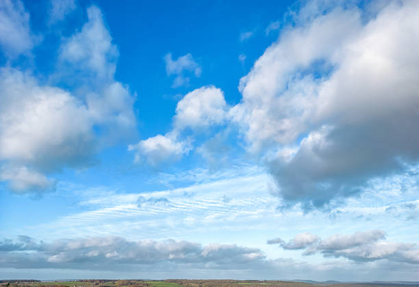 The sky is a vibrant blue, with soft white clouds drifting gently. Some clouds are thin and wispy, while others are thick and fluffy, creating a peaceful look.