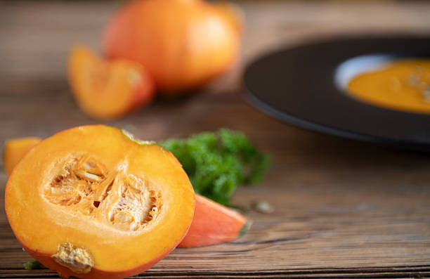 Ripe pumpkin cut in half with visible seeds on a wooden background. Autumn vegetable and cooking ingredient.