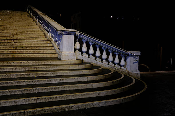 Night view of a historic stone bridge staircase in Venice, Italy. The curved steps and classical balustrade are illuminated against a dark background, creating a minimalist and atmospheric architectural scene. Concepts of solitude, timeless design, travel, and European heritage.