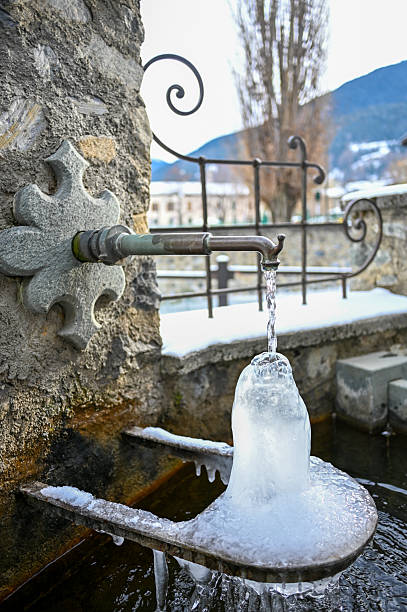 Water is continuously flowing from a stone fountain, forming ice during cold winter weather