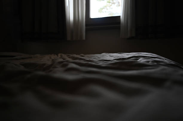 istock Empty rumpled bed in dark cozy bedroom with window light 2256300863