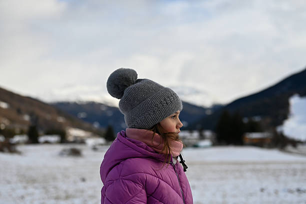 Little girl wearing a purple jacket and grey hat, enjoying outdoor nature on a winter day