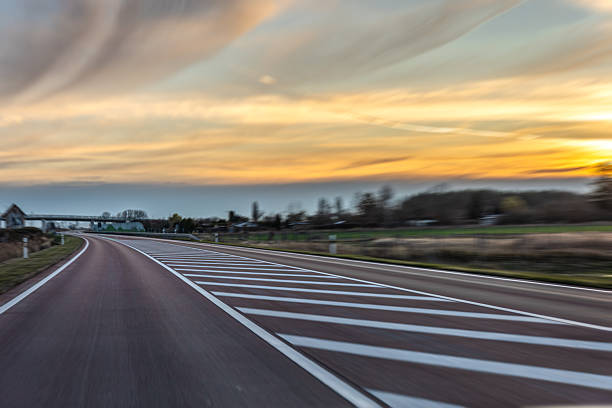 A smooth highway curve with bold markings cuts through open fields under a warm evening sky. Subtle motion blur creates a cinematic feel with generous copy space for modern design.