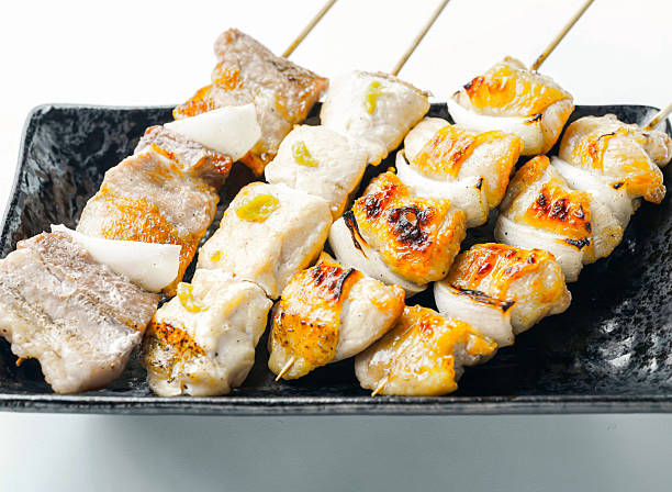 Grilled chicken skewers on a black plate, perfectly charred isolated on white background
