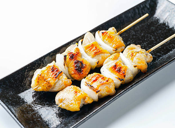 Grilled bird skewers with onions on a black plate isolated on white background