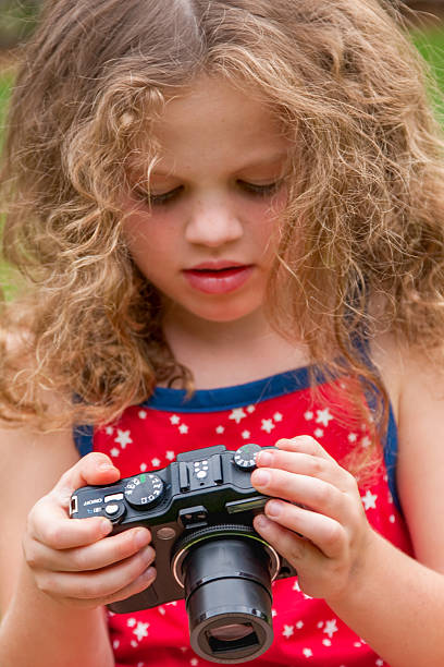 Cute girl looking intently at camera screen outdoors on summer day. Focus on foreground.
