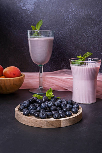 Mound of blueberries and a blueberry and avocado smoothie on a hickory wood table