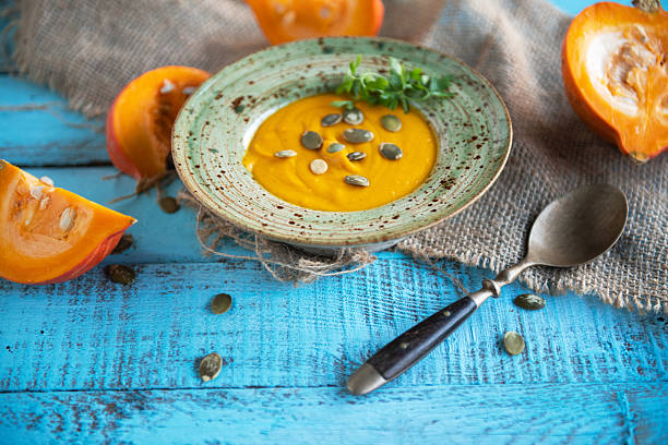 A bowl of creamy autumn pumpkin soup garnished with pumpkin seeds and herbs, served on a vintage wooden background with fresh pumpkins.
