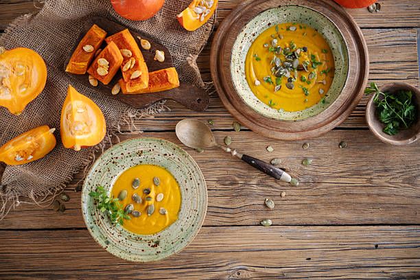 A bowl of creamy autumn pumpkin soup garnished with pumpkin seeds and herbs, served on a vintage wooden background with fresh pumpkins.