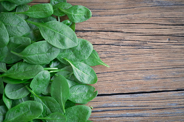 A pile of organic baby spinach leaves rich in vitamins, spread over a dark rustic wooden surface.