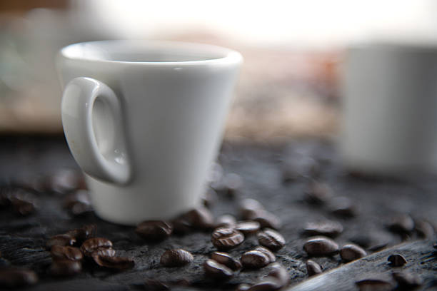A top-down view of a steaming cup of espresso or black coffee placed on a pile of roasted aromatic coffee beans.