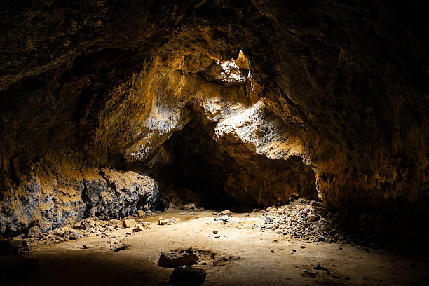 Sunlight enters through ceiling openings illuminating the interior of a lava tube cave in the Mojave Desert