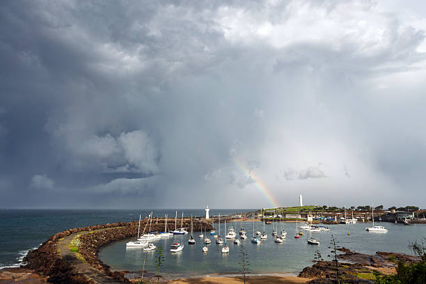 Huge ominous storm clouds fill a dramatic sky with a distant rainbow above the iconic Belmore Basin and Wollongong Harbour featuring the famous dual lighthouses on the headland and breakwall. Captured from a high perspective during a storm event.