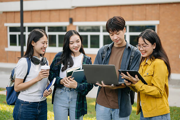 istock Asian Students are studying the campus park. Young people are spending time together. Reading book, working with laptop and tablet sitting on stairs 2256354859