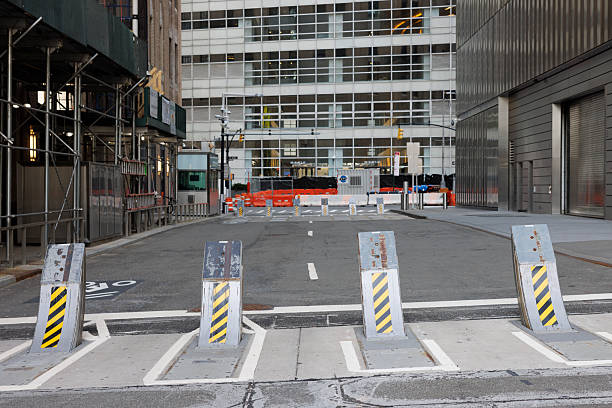 New York, New York, USA - March 23, 2025: A row of four retractable anti-ram security bollards blocking vehicle access to an empty street in Manhattan. In the background, modern office buildings line the street, with one structure covered in construction scaffolding.