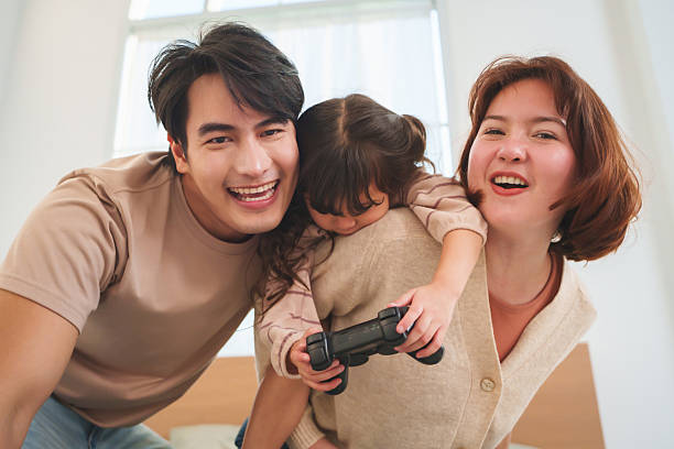 Asian family enjoys playful moment with parents and little girl laughing together in living room