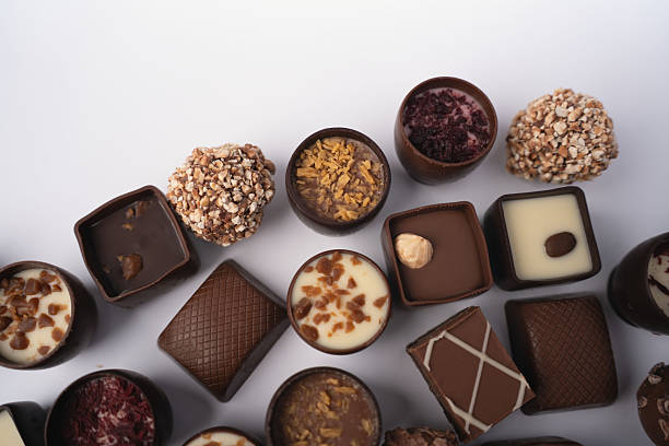 close-up flatlay of assorted gourmet chocolates and truffles on a white backdrop, showcasing varied textures, nuts, ganache and creamy fillings; elegant, indulgent presentation with warm brown tones