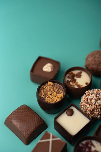close-up of assorted gourmet chocolates and truffles arranged on a teal tabletop, featuring dark and white chocolate cups, crunchy nut coatings, sprinkled toppings, creamy ganache and indulgent mood