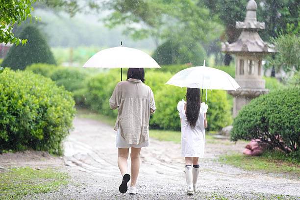 Two women walking in the rain, one holding an umbrella and the other holding an umbrella as well