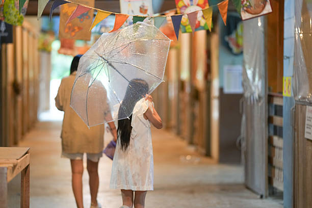 A girl is walking down a hallway with a clear umbrella. The scene is set in a building with a banner hanging from the ceiling
