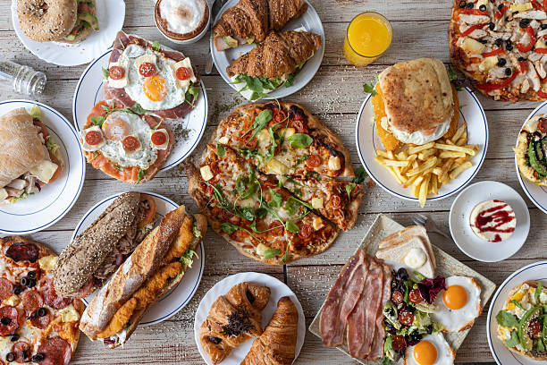 Table full of various delectable dishes, featuring pizzas, sandwiches, croissants, and fried eggs