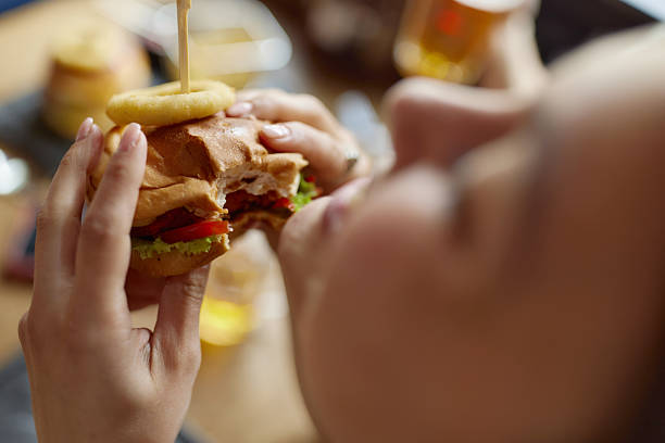 Close up of unrecognizable woman eating cheeseburger.