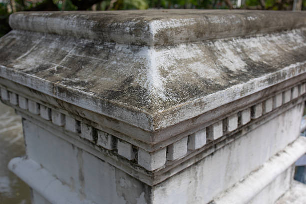 Square base of an old white stone column with traces of black mold
