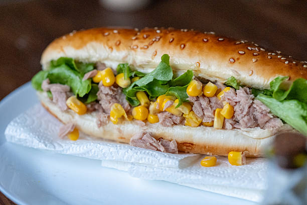 Close-up view of a tuna sandwich filled with corn and fresh greens. The image highlights healthy lunch choices, homemade food, and simple Mediterranean-inspired ingredients.