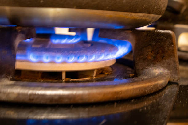 Flames burn in a blue hue on a gas stove. The kitchen is dimly lit as food is being cooked. The atmosphere shows a moment of preparation for a meal.
