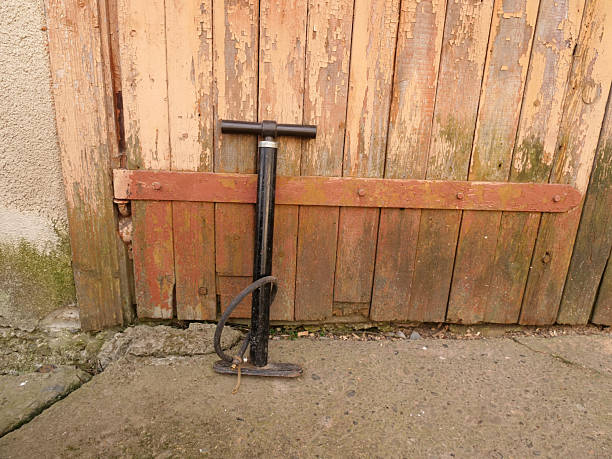 Manual bicycle pump standing against old peeling wooden gate in yard.
