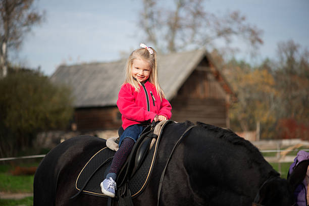 Horizontal image showing young children riding a calm black horse during a supervised learning moment. Warm autumn colors support themes of child development, trust, balance, and emotional growth.