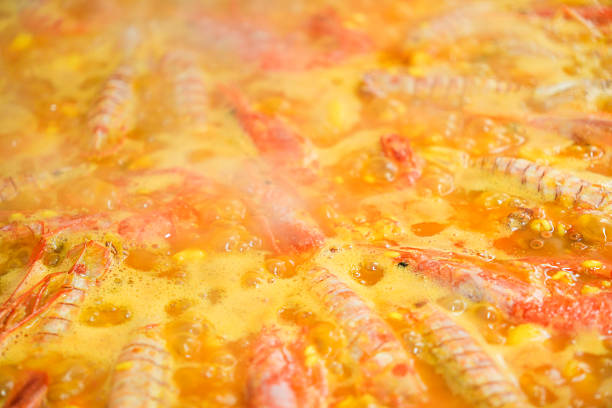 A pot of food with shrimp and corn in it. The food is yellow and bubbling. The shrimp are cooked and floating in the broth