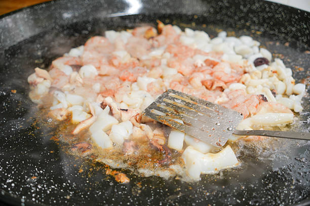 A pan of food is being cooked with a spatula. The food is a mix of shrimp and other ingredients