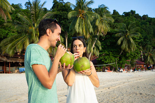 Couple celebrating tropical vacation on beach drinking coconut water