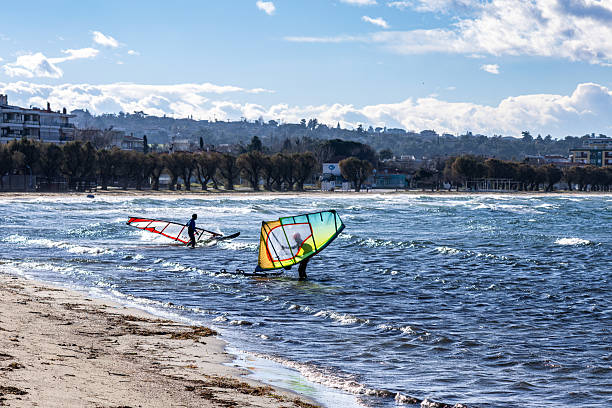 Windsurfer gliding at high speed on the Étang de Salses-Leucate against a picturesque coastal backdrop of residential houses and waves of water illuminated by the evening sunlight on a windy day.