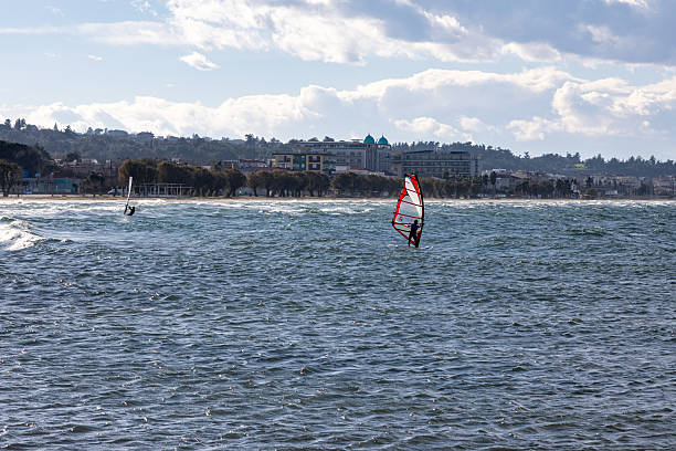 Thermaikos, Greece – 8 January 2026: Windsurfers ride strong winter winds on choppy waters near the Greek coastline as cold weather creates rough sea conditions. Despite low temperatures, water sports enthusiasts continue training and recreational activities, highlighting year-round coastal life in Greece.