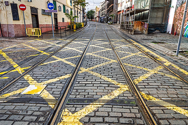 Santa Cruz, Tenerife, Spain, Europe - December 14th 2025: A road intersection in Santa Cruz, the main city of Tenerife in the Canary Islands, features tram tracks and prominent yellow road markings indicating that vehicles must keep the area clear. The scene documents everyday urban traffic management designed to ensure unobstructed passage for the city’s tram system.