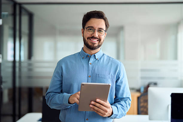istock Smiling young business man manager with tab standing in office. Portrait. 2256413541