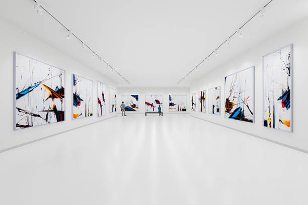 The interior of a modern and minimalist art gallery. The floors and walls are white, with large abstract expressionist paintings in black, blue, yellow, and red hanging on the white walls. A man and a woman are looking at the paintings.