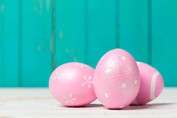 Pink eggs with decorative designs are placed on a light wooden surface against a blue background.